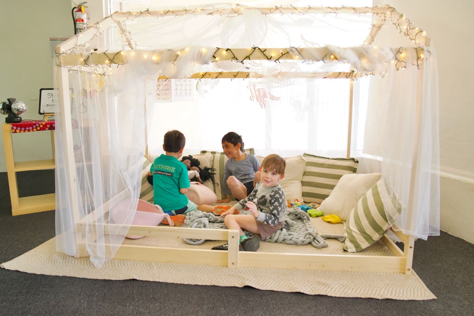 Three children gathered in the fairy-lit reading tent at Guthrie Street Child Care