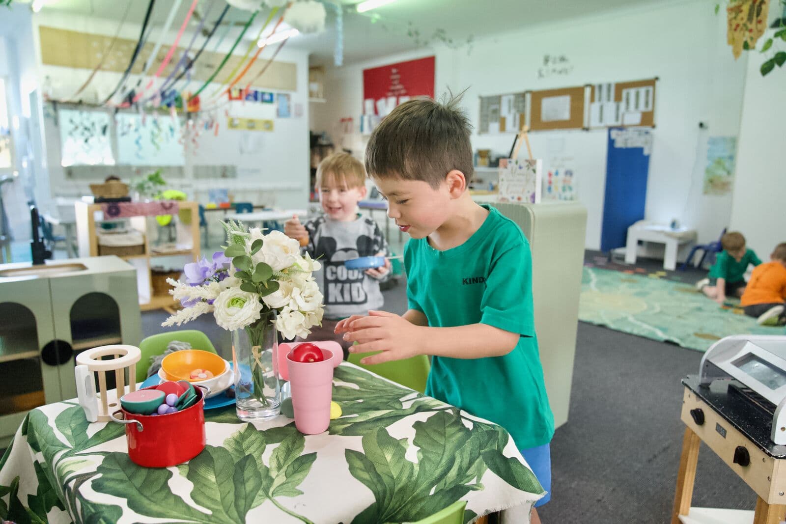 Two children at the kitchen table with flowers and play utensils at Guthrie Street Child Care