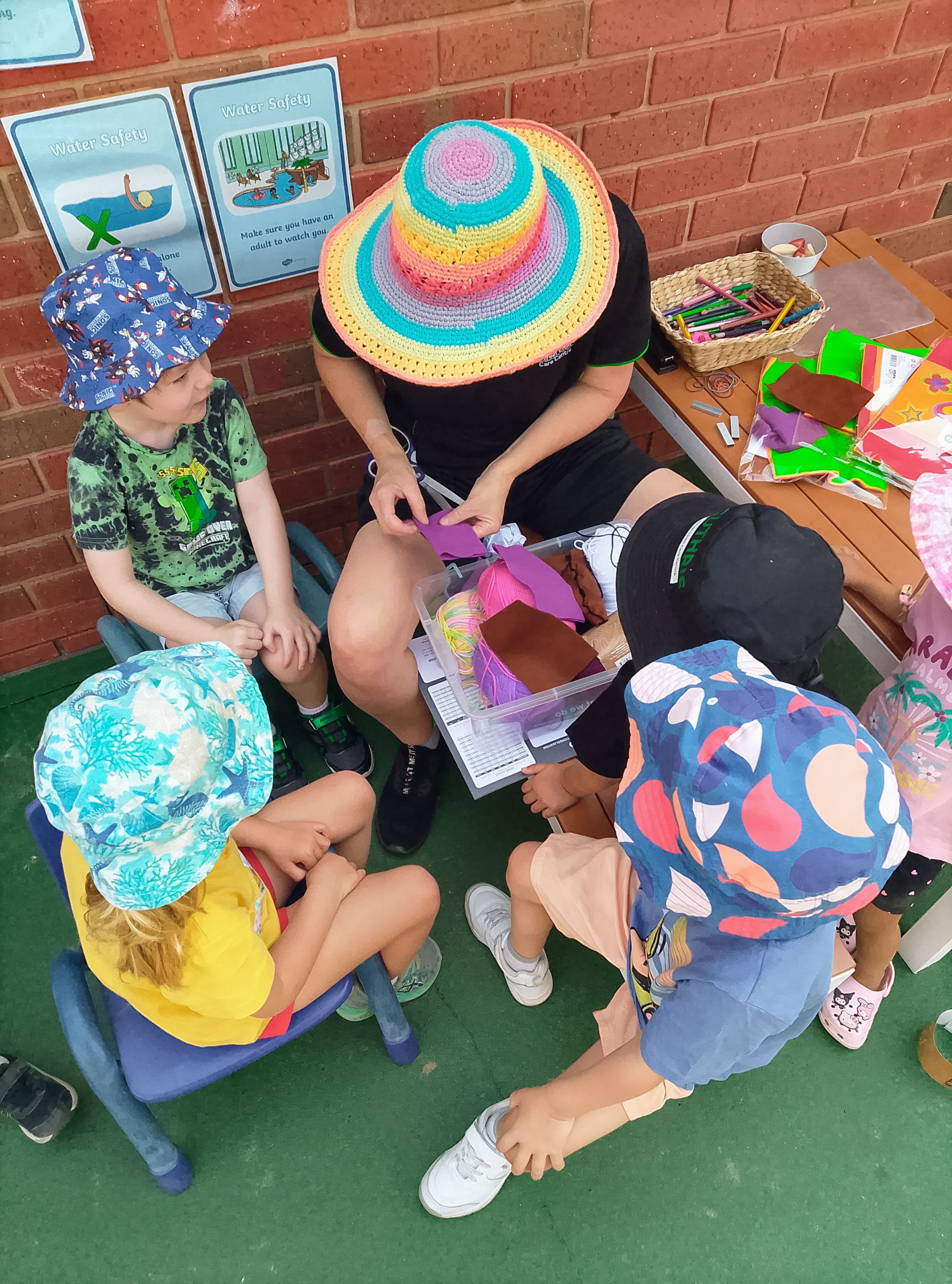 An educator sitting with children doing a craft activity in the outdoor yard at Guthrie Street